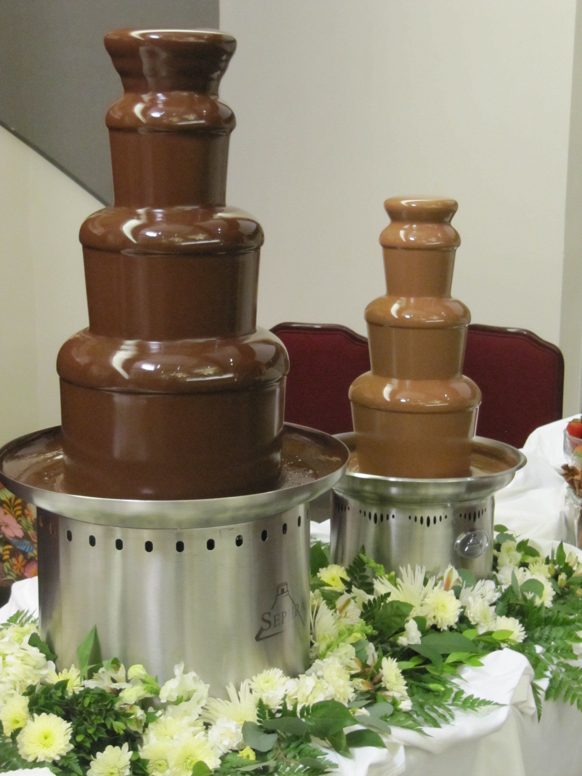 Two chocolate fountains are sitting on a table with flowers
