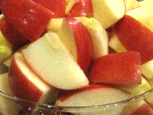 A glass bowl filled with sliced apples on a table.