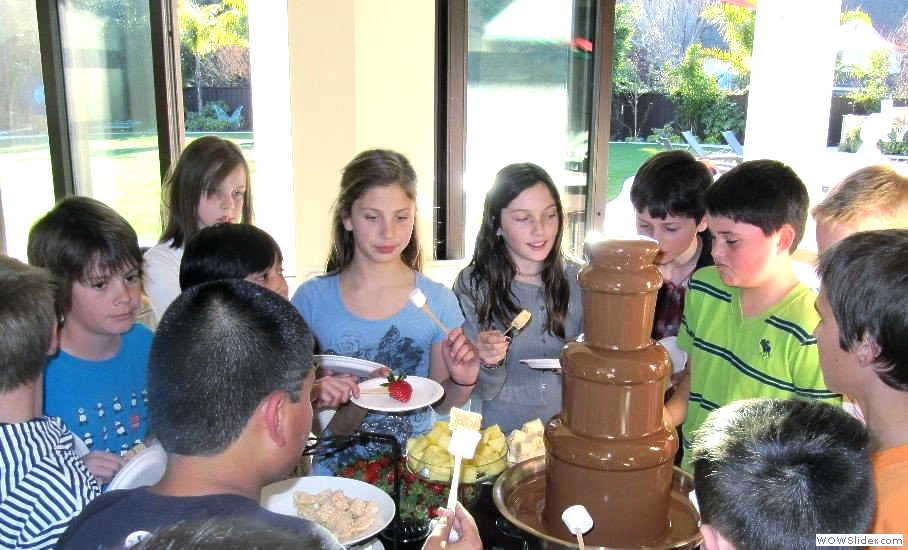 A group of children are sitting around a chocolate fountain
