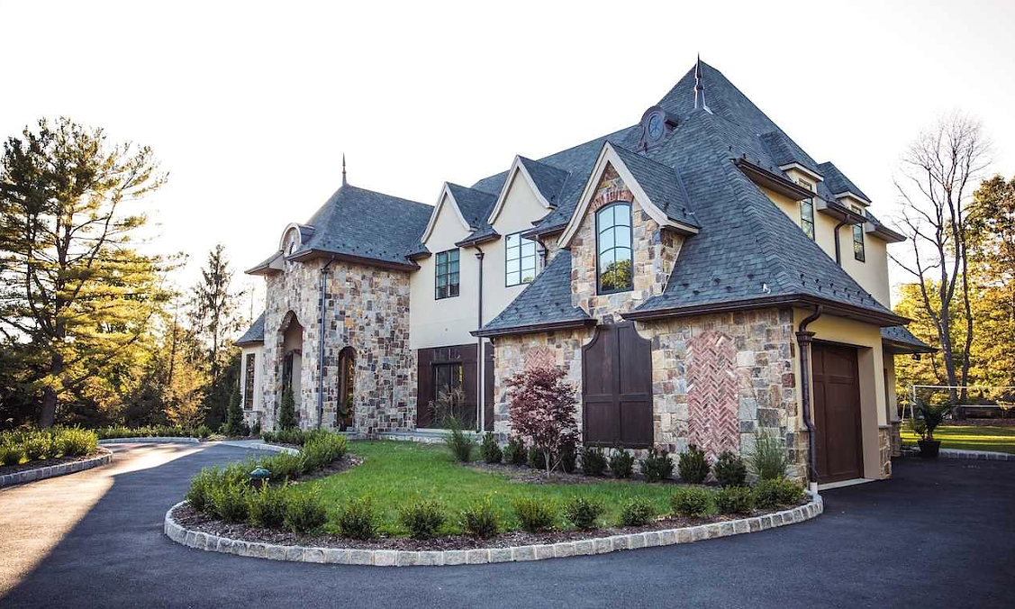 A large stone house with a gray roof is sitting on top of a lush green hillside.