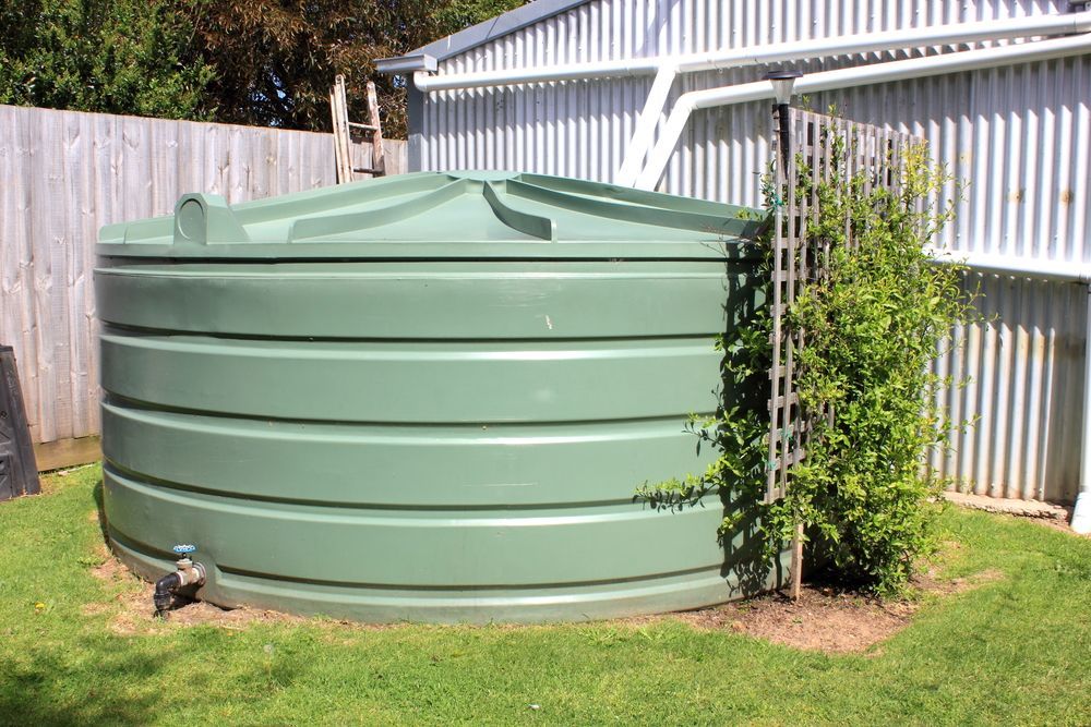 A green water tank is sitting in the grass in front of a building  — Elite Water In Lismore, NSW