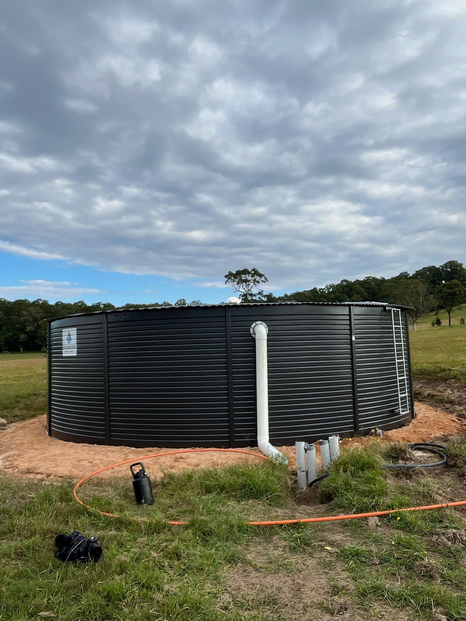 A Large Black Water Tank is Sitting in the Middle of a Grassy Field — Elite Water In Koonorigan, NSW
