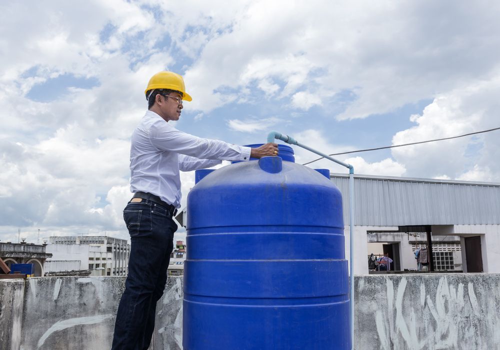 A Man is Standing on Top of a Blue Water Tank on a Roof — Elite Water In Lismore, NSW