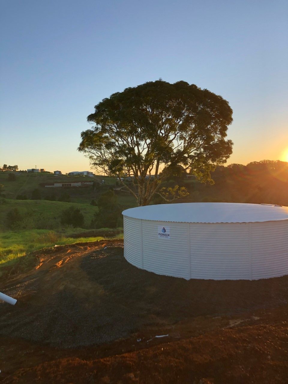 A Large White Tank is Sitting in the Middle of a Field With a Tree — Elite Water In Koonorigan, NSW