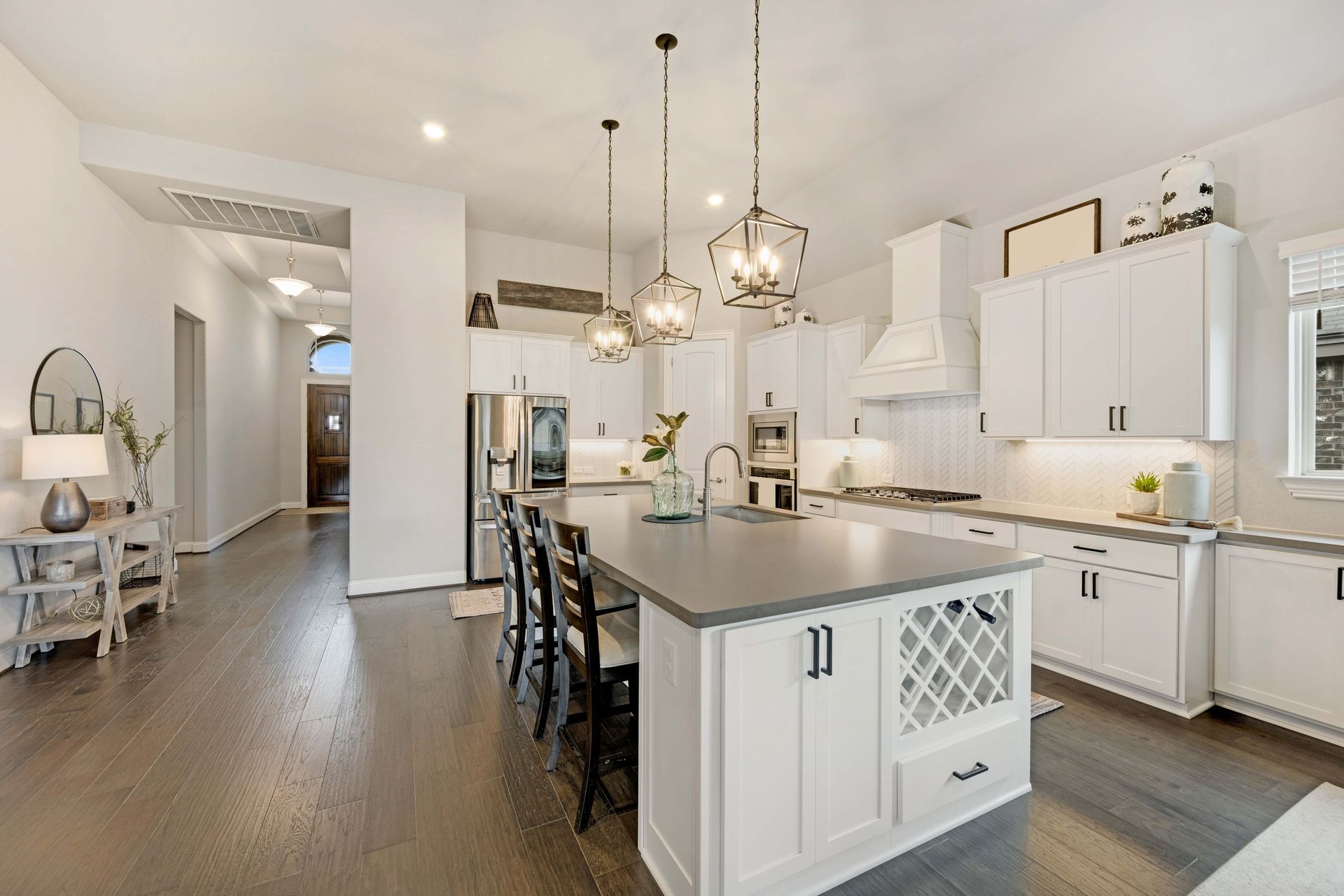 Spacious white kitchen with dark wood floors, island, and cabinets. Pendant lights hang above the island.