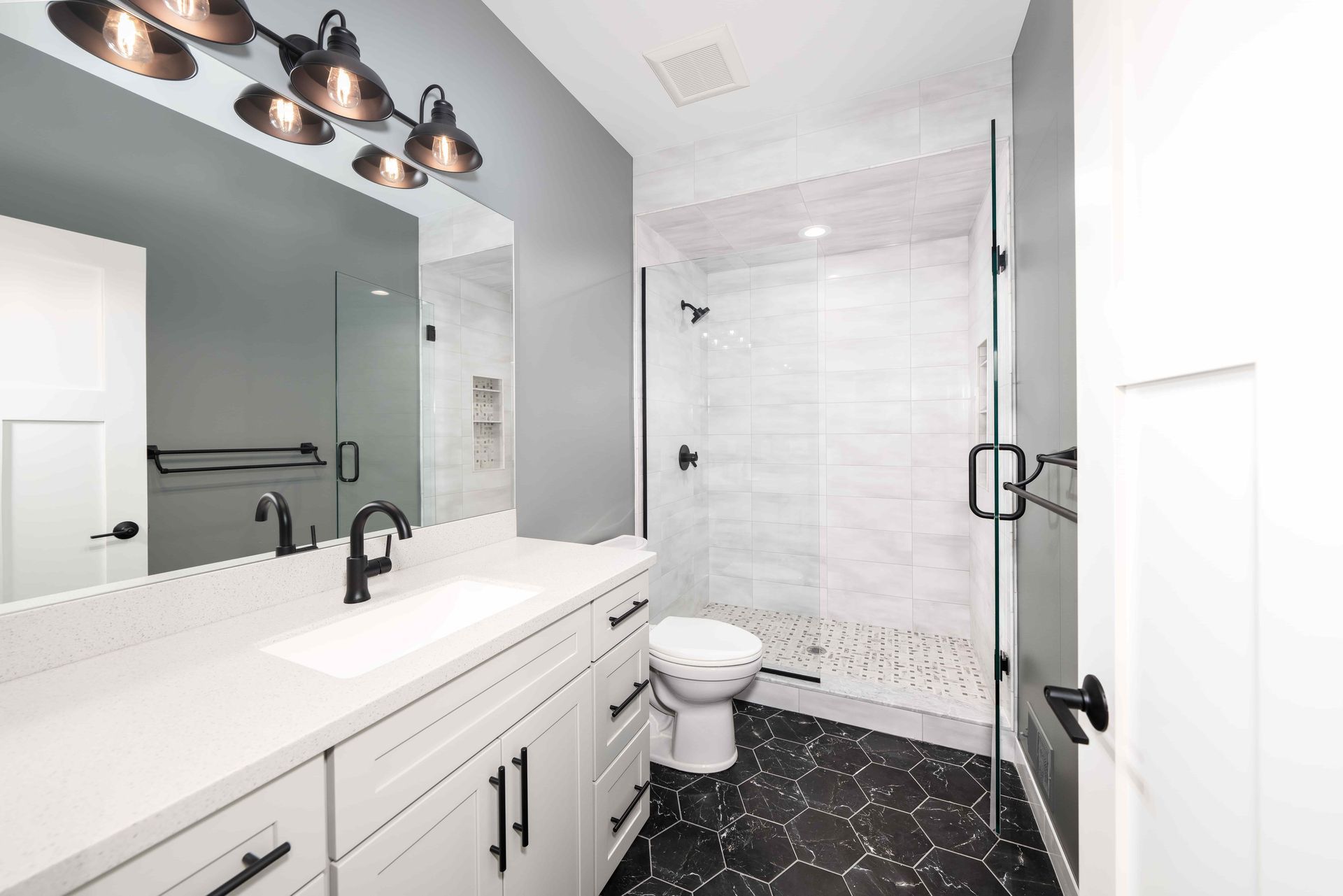 Modern bathroom with white cabinets, gray walls, and black hexagonal floor tiles.