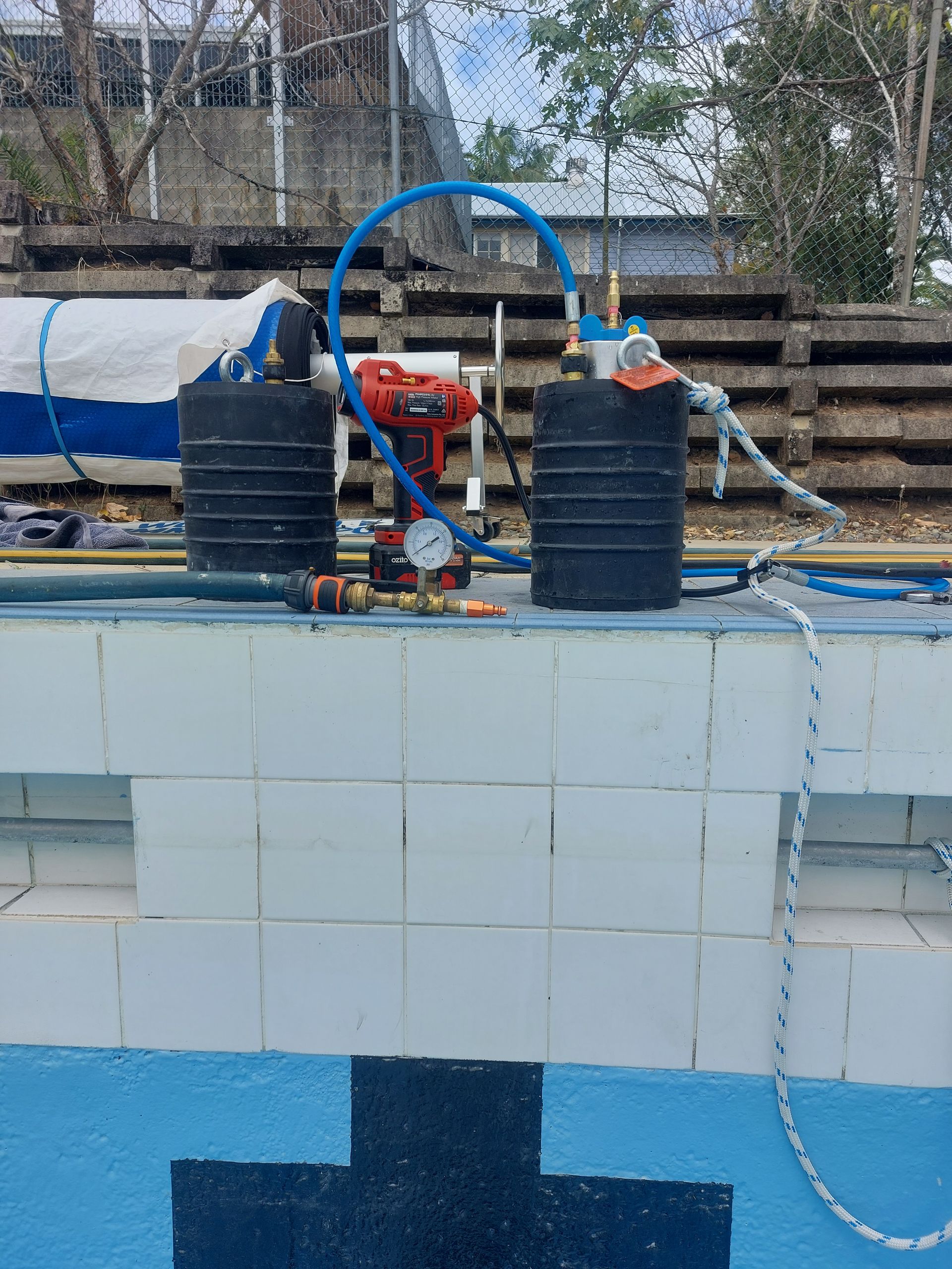 Equipment set up on the edge of a swimming pool, likely for leak detection or repair.