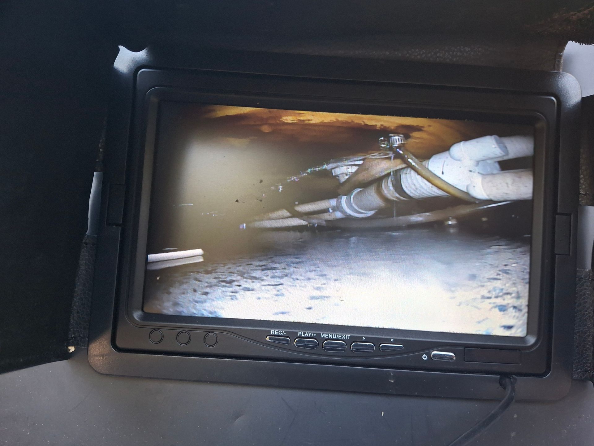 Monitor displaying a view inside a crawlspace showing pipes, dampness, and possible mold.