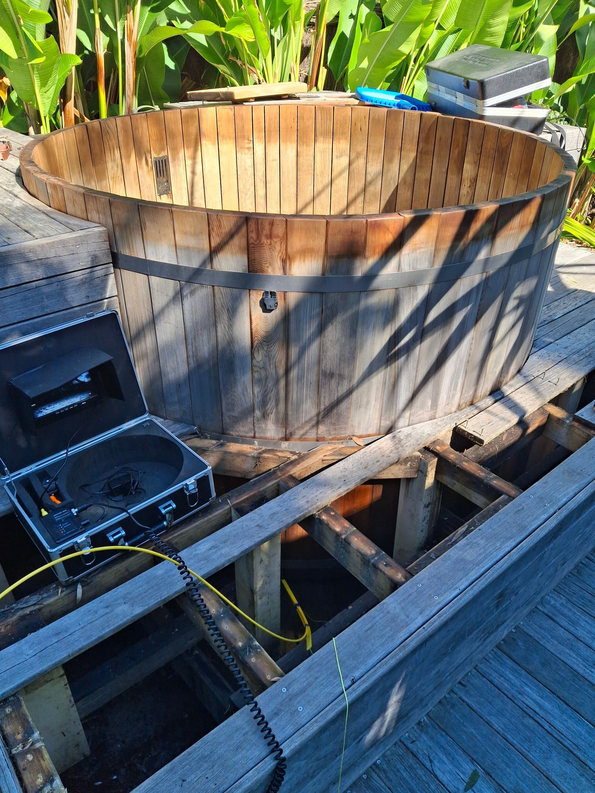 Wooden hot tub on a deck with an open access panel revealing supports and equipment.