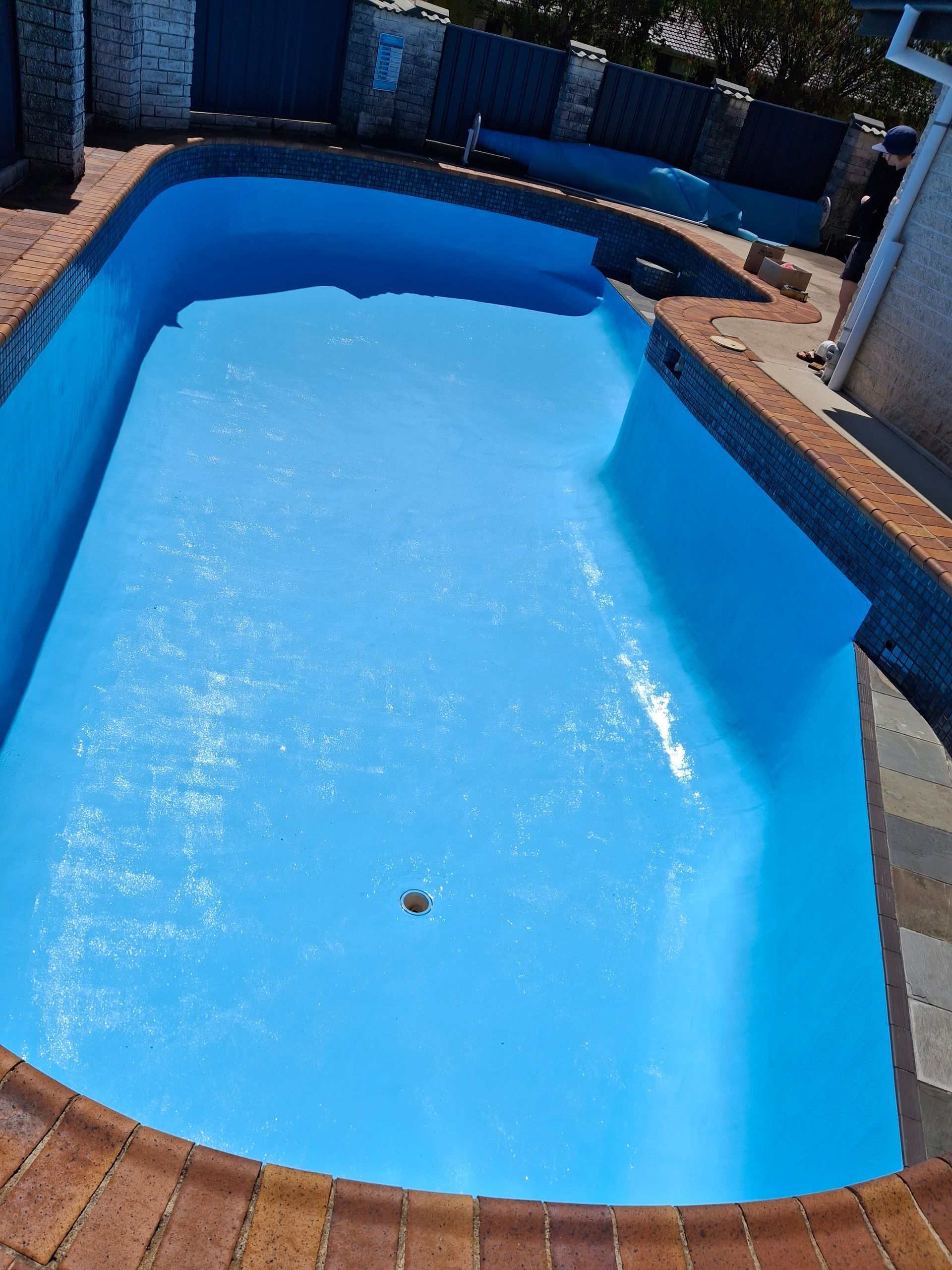 Blue, empty swimming pool, surrounded by brick and concrete, outdoors.