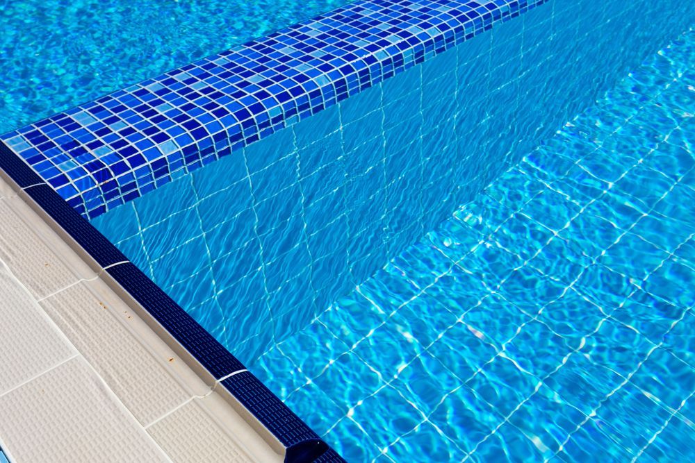 Pool Edge With Blue Tiled Border and Water Reflections — Ballina Leak Detection & Swimming Pool Repairs in Ballina, NSW