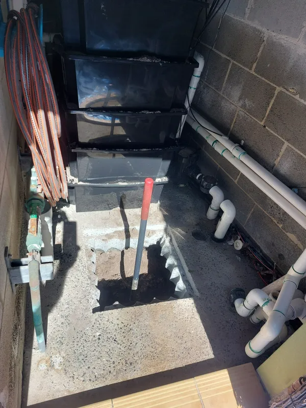 Outdoor stairwell with metal steps, water pipes, and a lever against a cinder block wall.