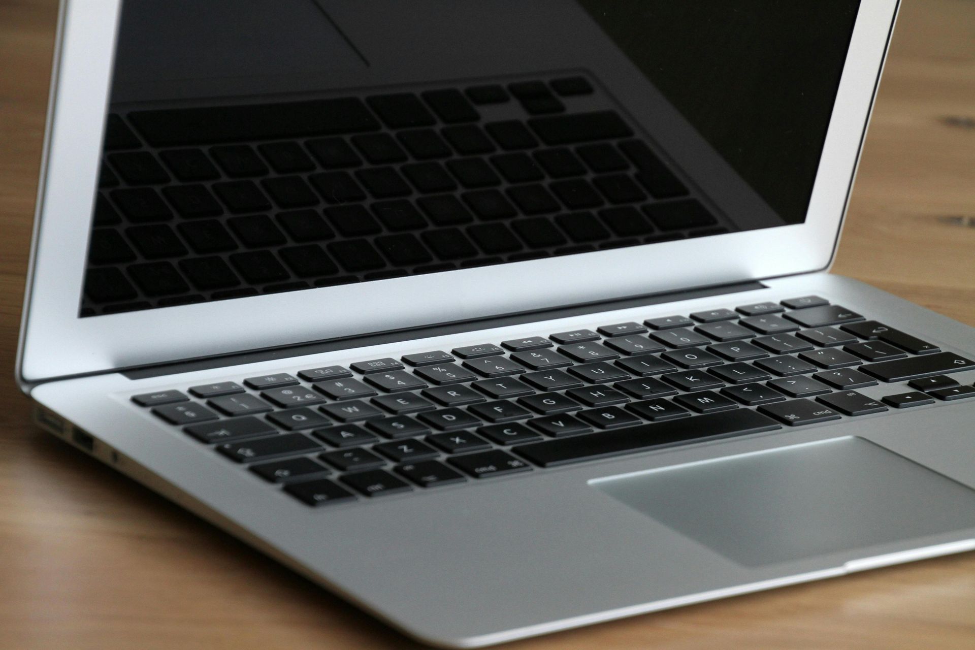 Silver laptop open on a wooden desk, showing a black screen and keyboard area
