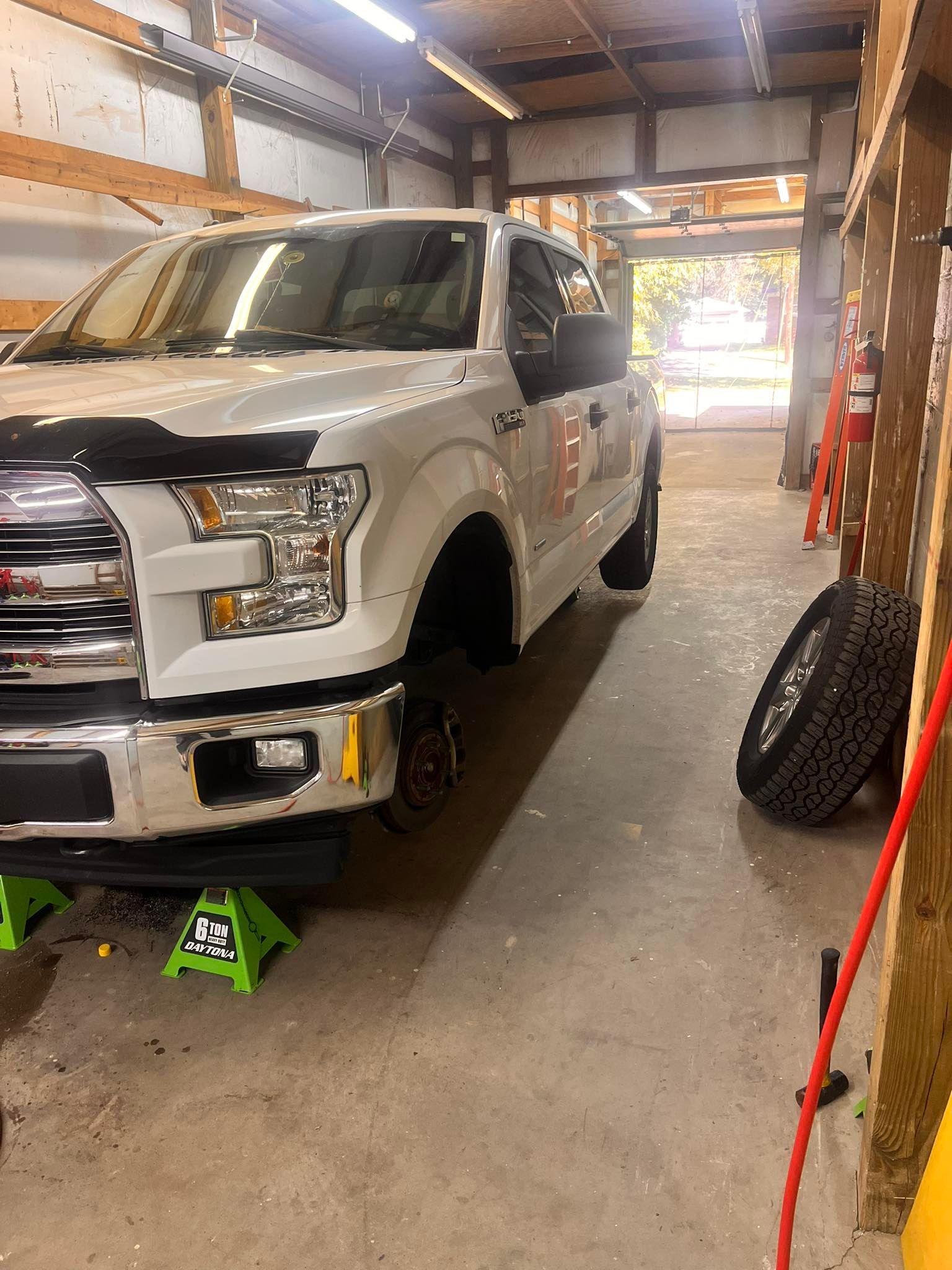 White pickup truck on jack stands inside a garage. One tire is leaning nearby.