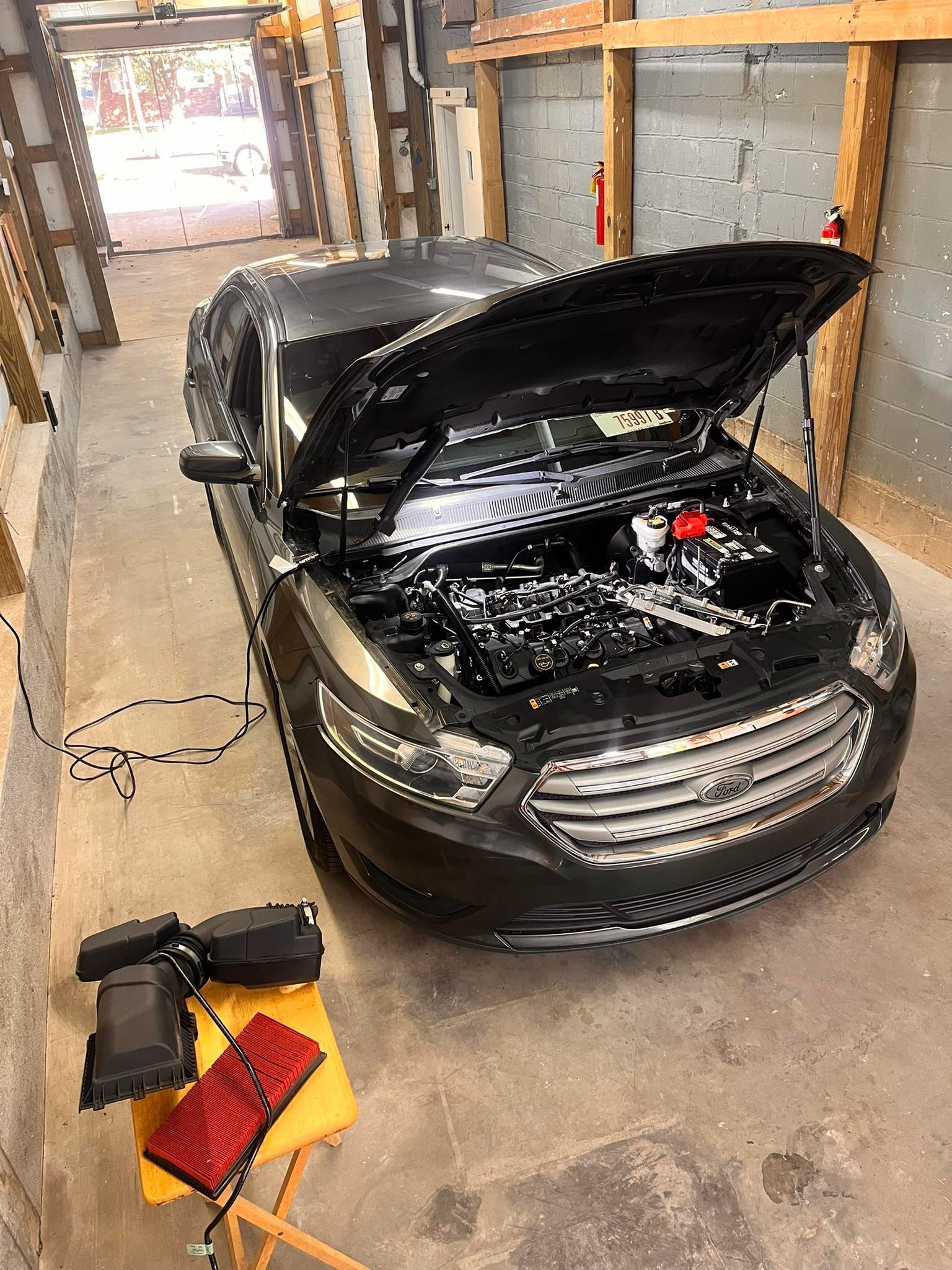 Black car with hood open in a garage, tools in the foreground.
