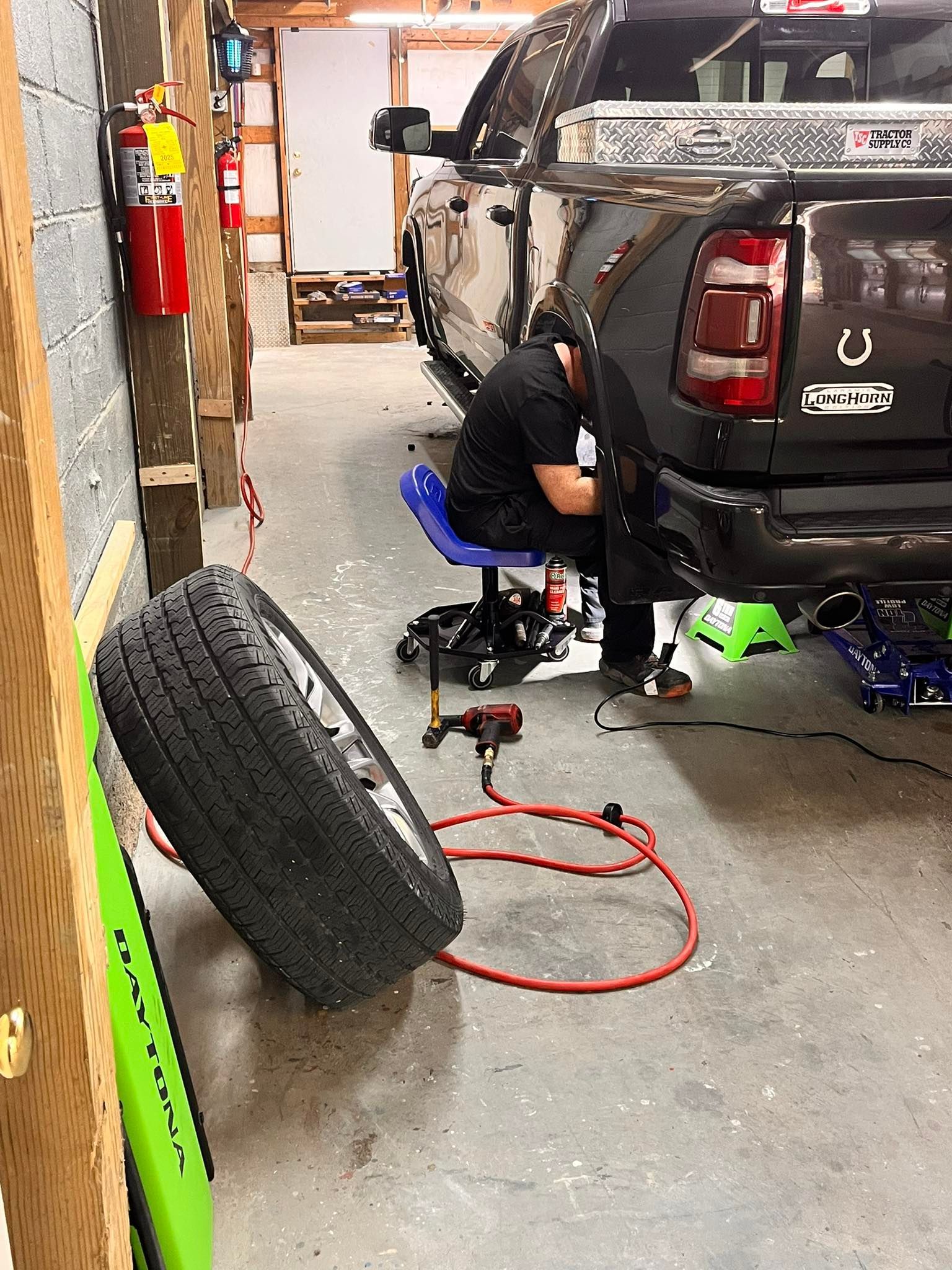 Mechanic working on a black truck in a garage; a tire is leaning against the wall.