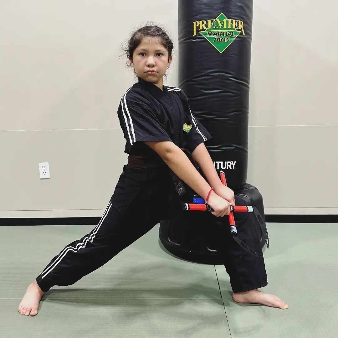 A young girl in a karate uniform is sitting on the floor.