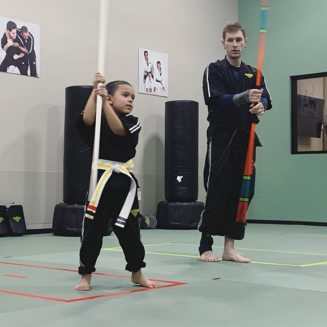 A group of children are practicing karate with a teacher in a gym.