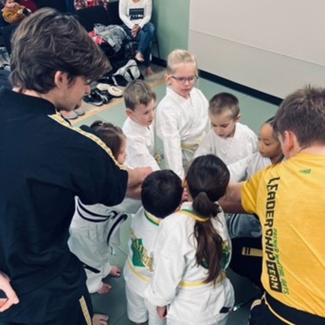 A man is kneeling down next to a young boy in a taekwondo class.
