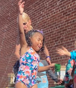 A little girl in a bathing suit is standing in front of a brick wall.