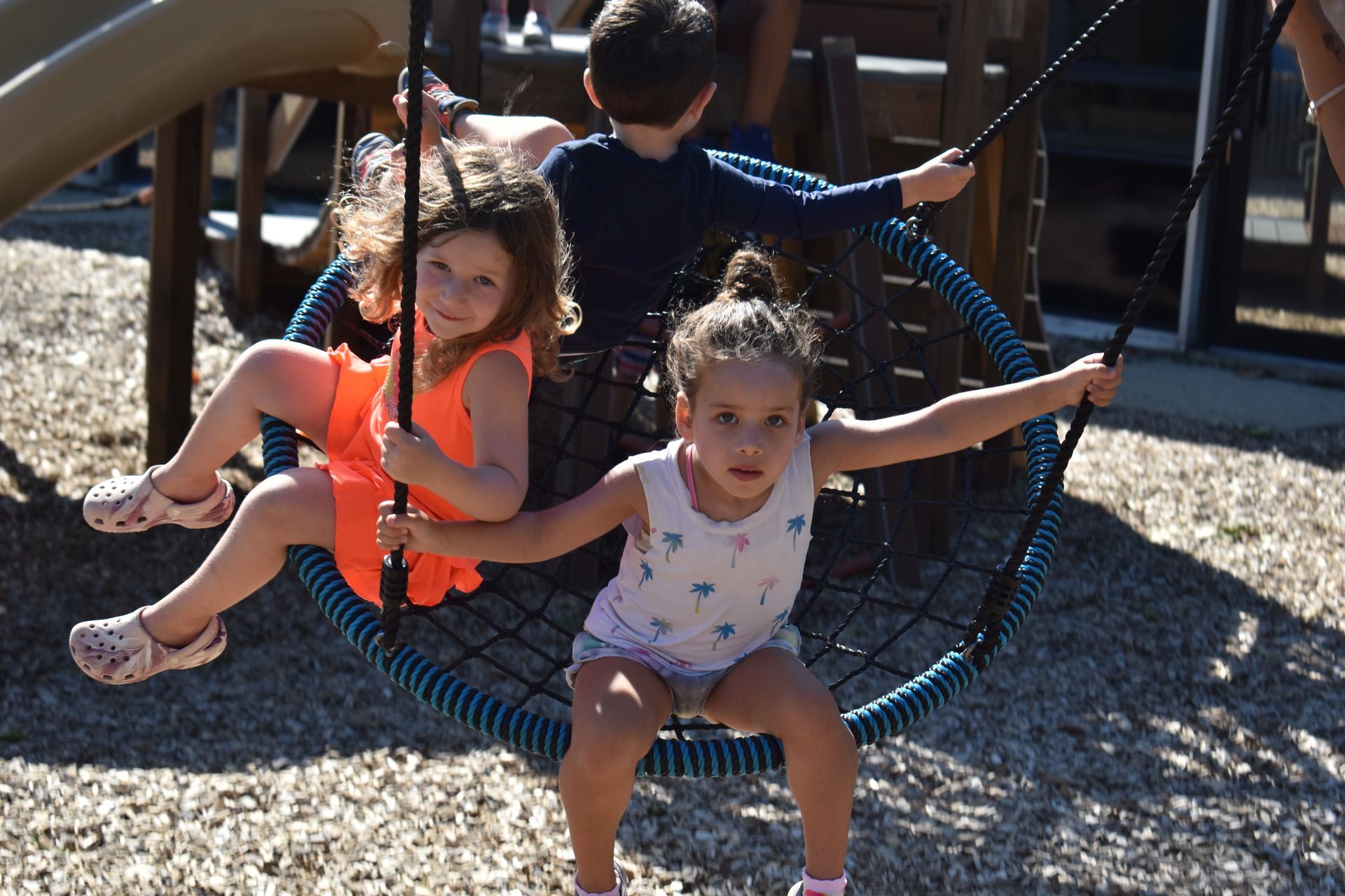 Two little girls are sitting on a swing in a playground.