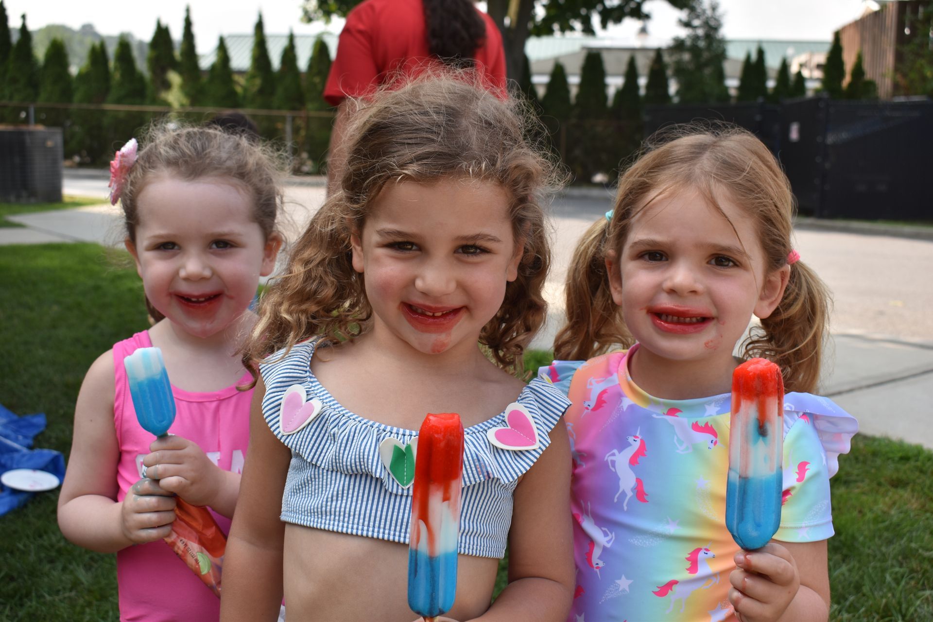 Three little girls are standing next to each other holding popsicles.