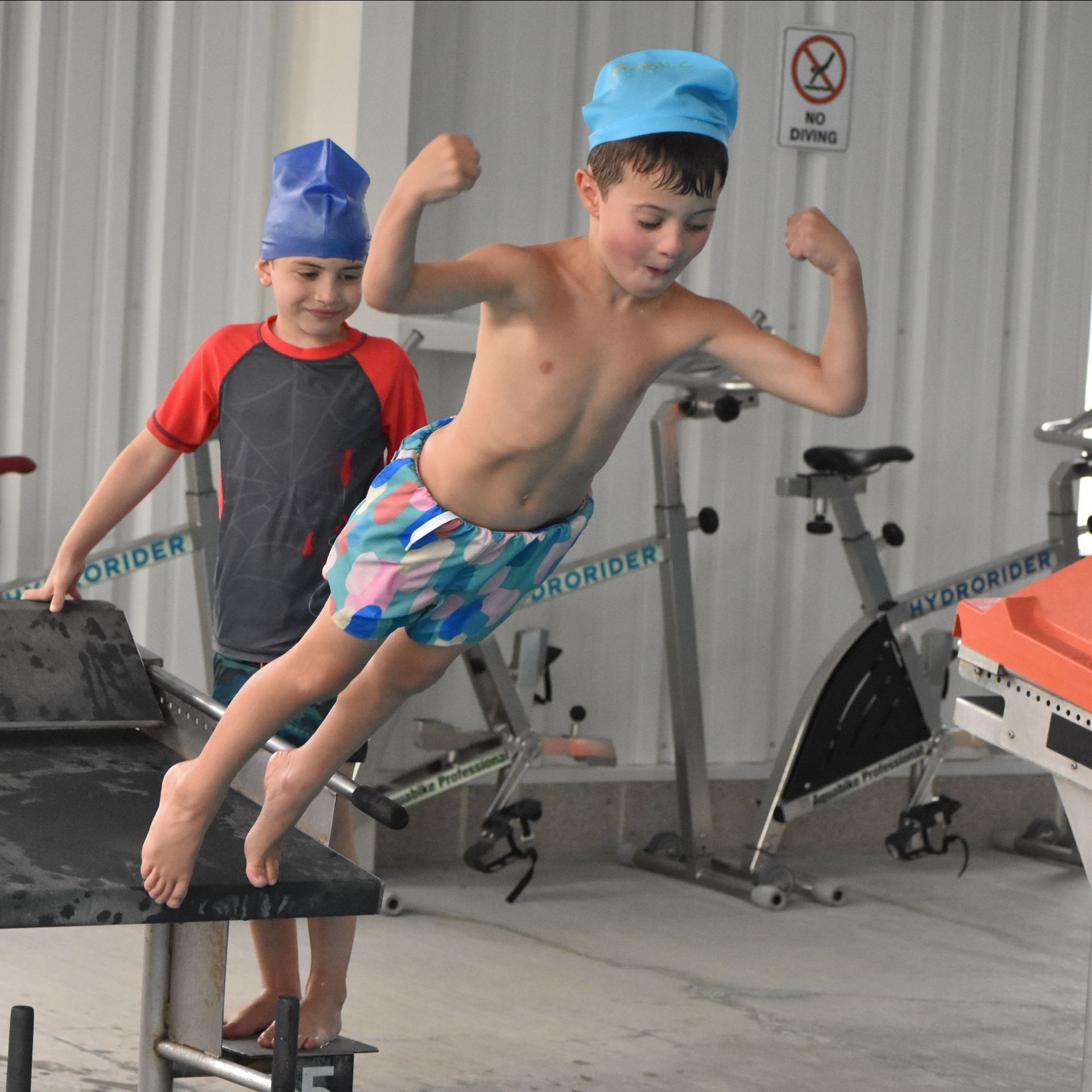 A boy is jumping into a pool while another boy watches