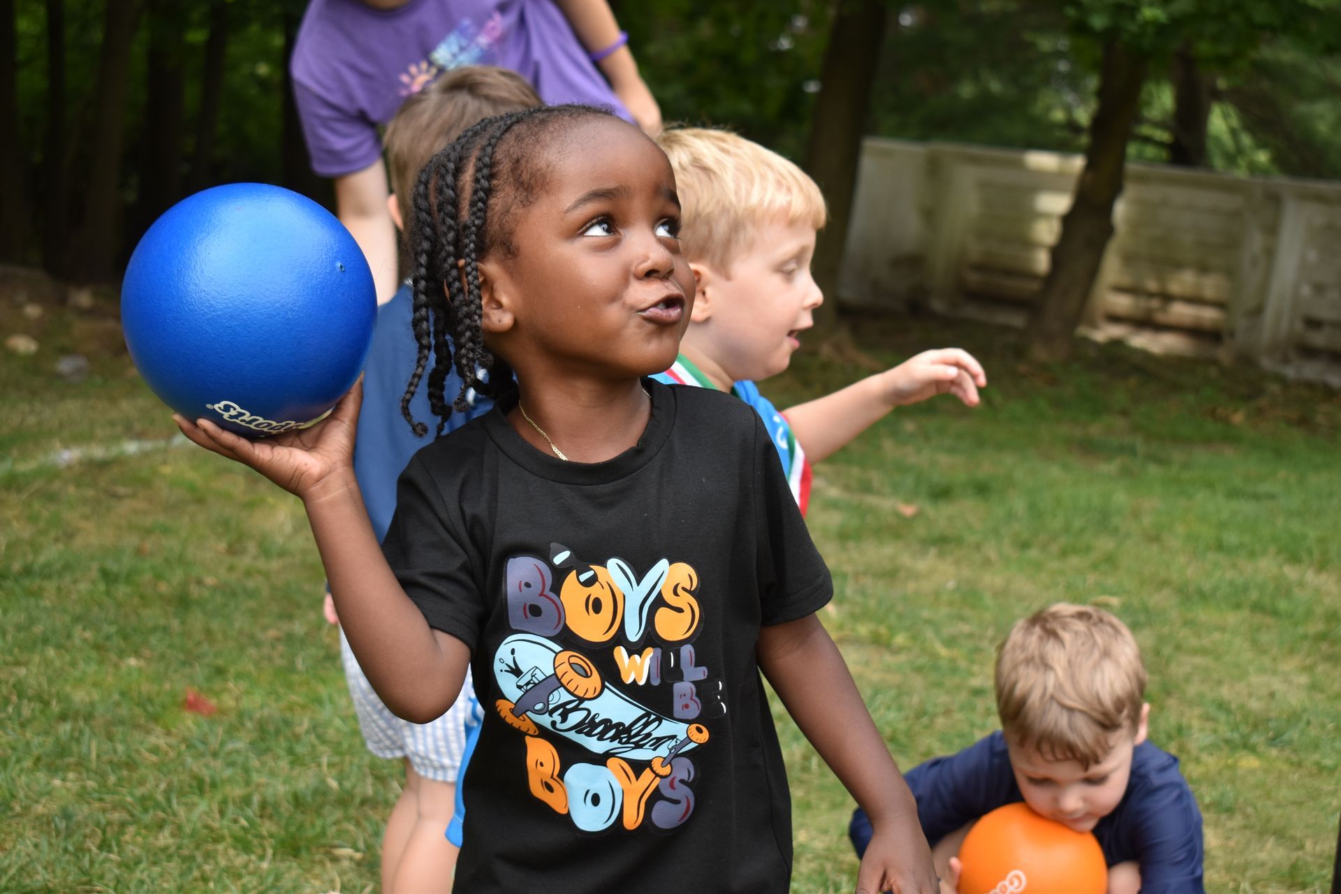 A girl wearing a black shirt that says boys own toys is holding a blue ball