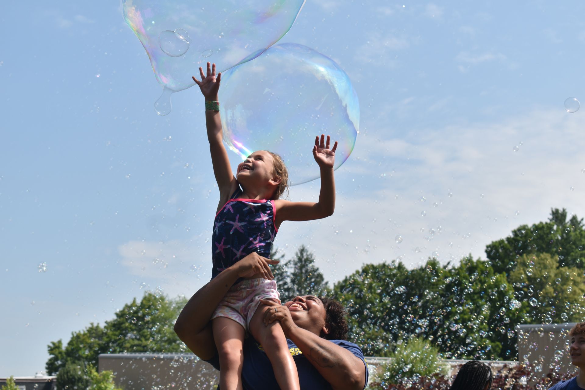 A man is holding a little girl in his arms while playing with soap bubbles.