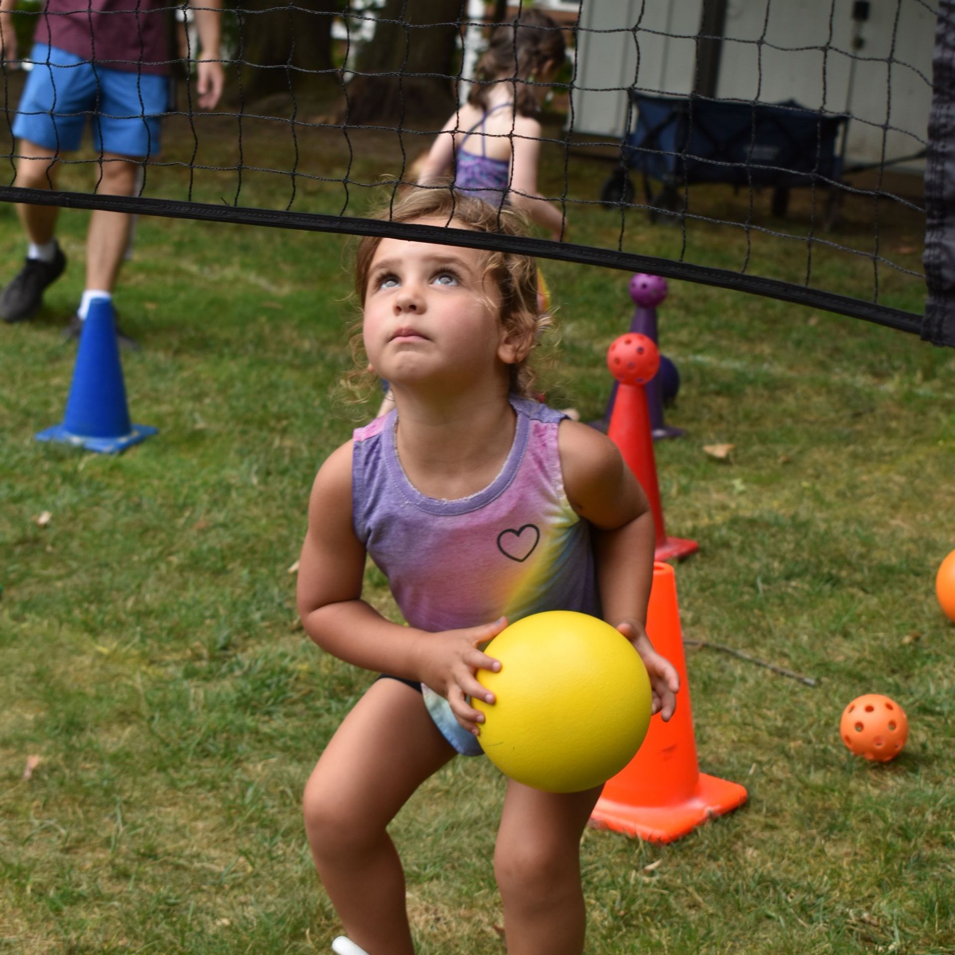 A little girl is holding a yellow ball in front of a volleyball net