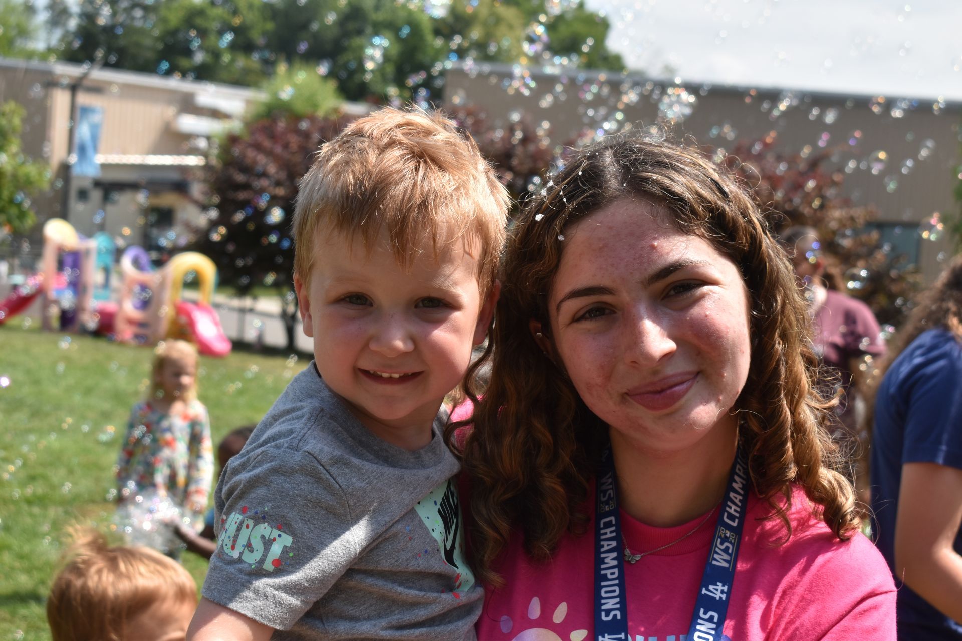 A woman is holding a little boy in her arms while bubbles are flying around them.
