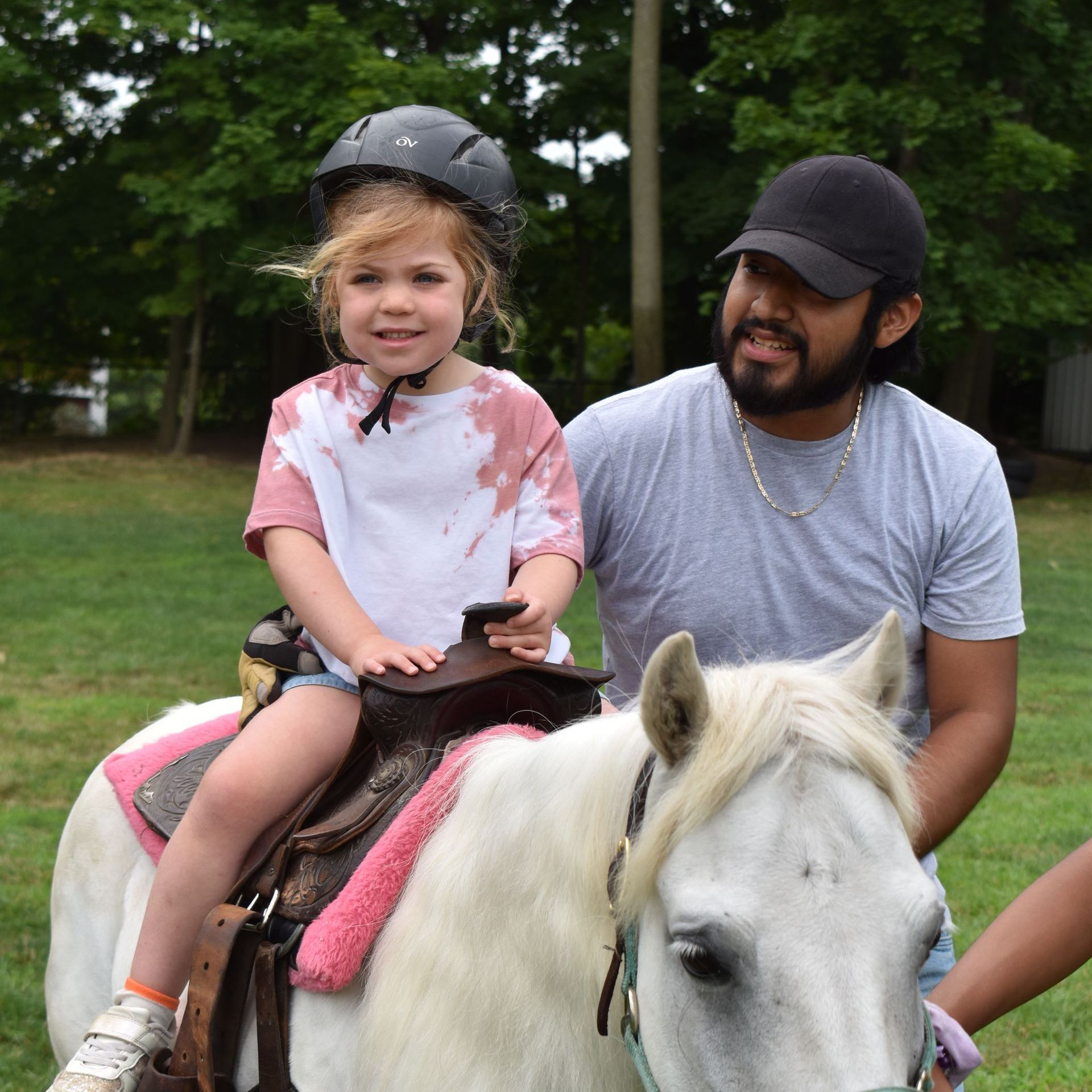 A little girl wearing a helmet is riding a white horse
