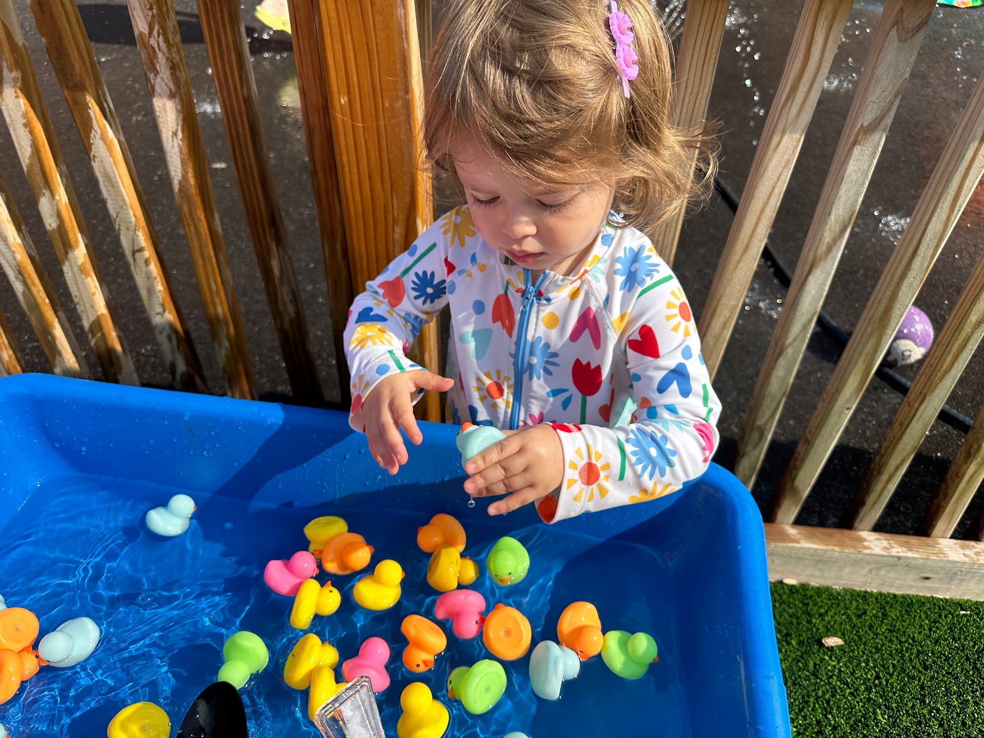 A little girl is playing with rubber ducks in a blue bin.
