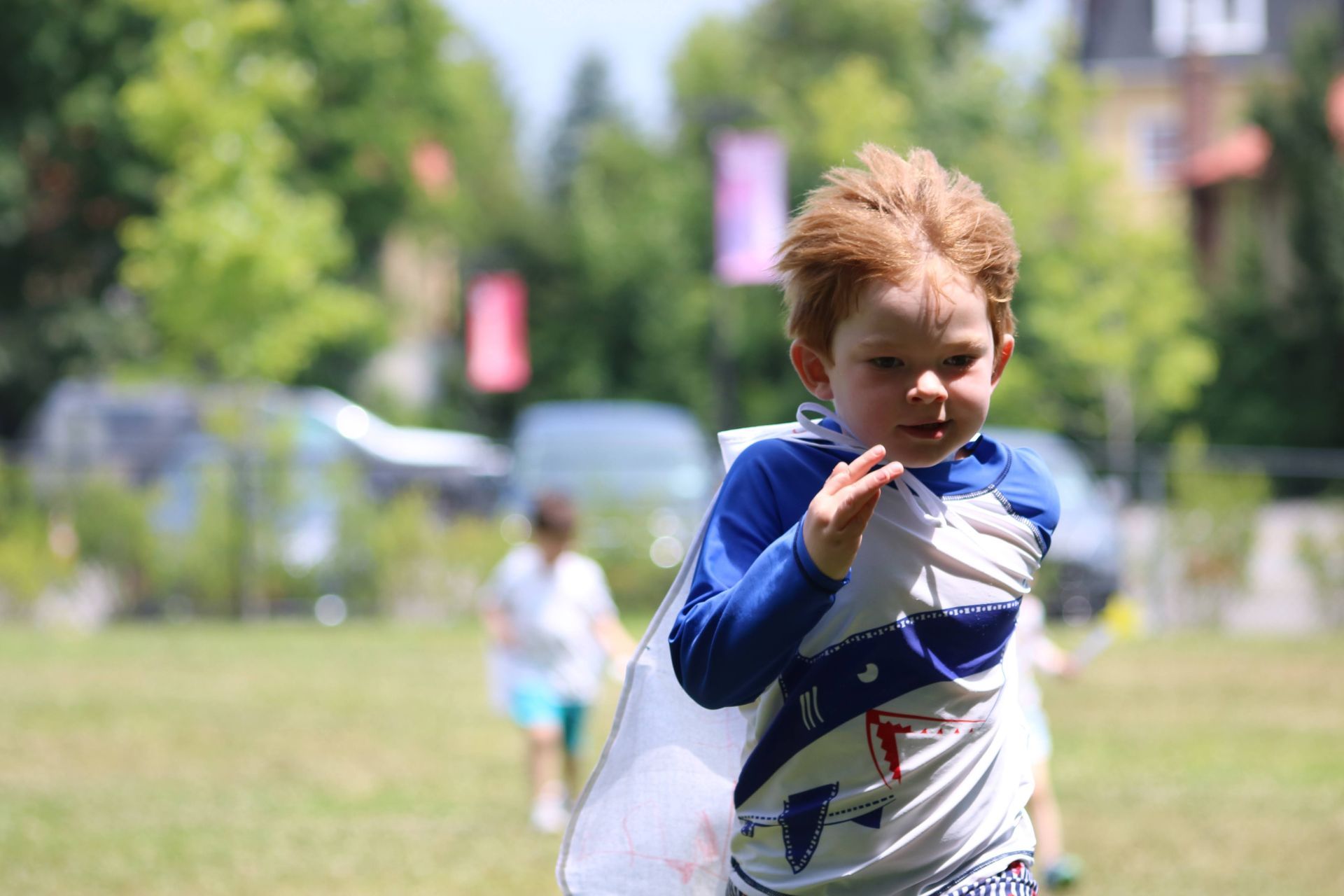 A young boy wearing a superhero cape is running in a field.