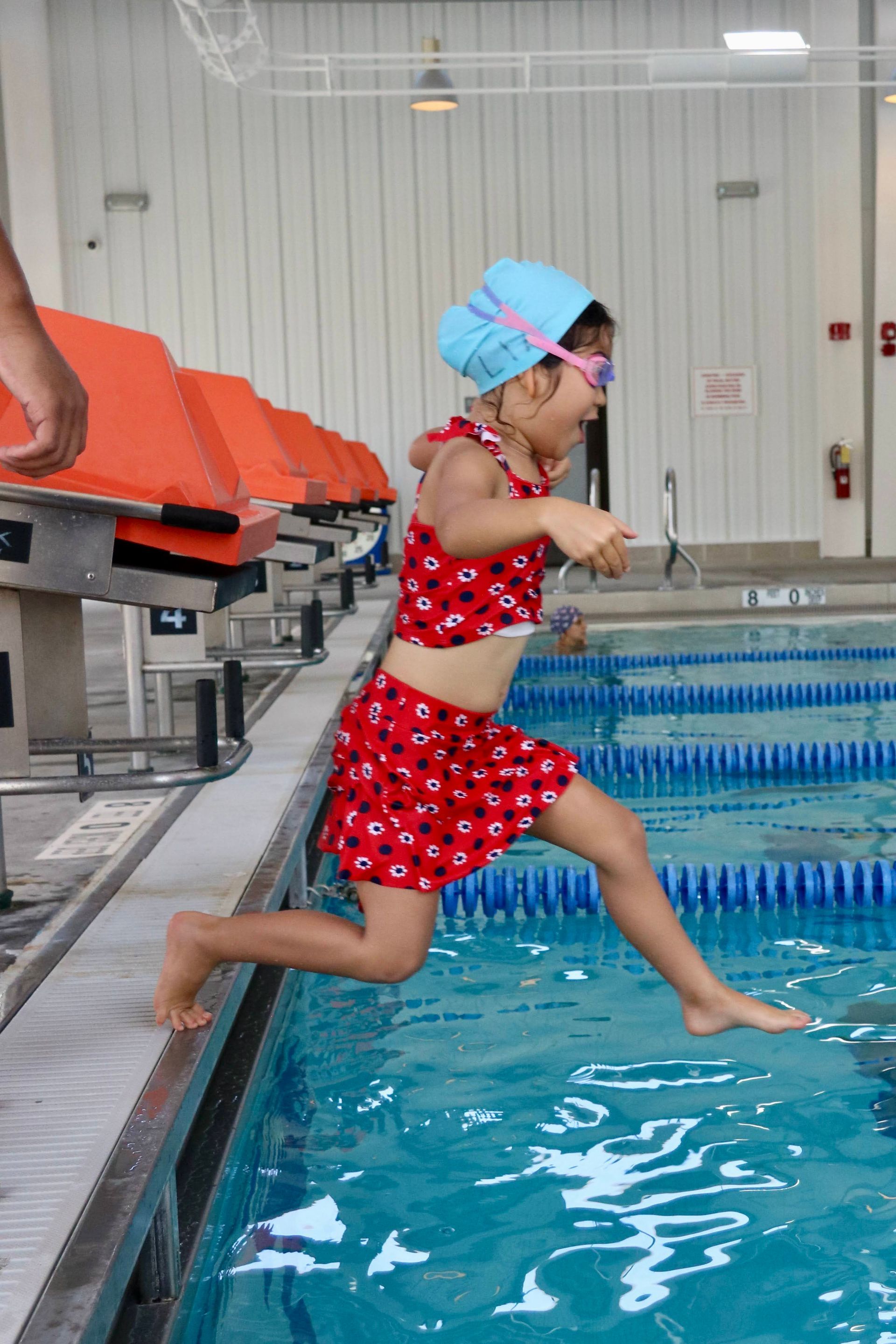 A little girl is jumping into a swimming pool