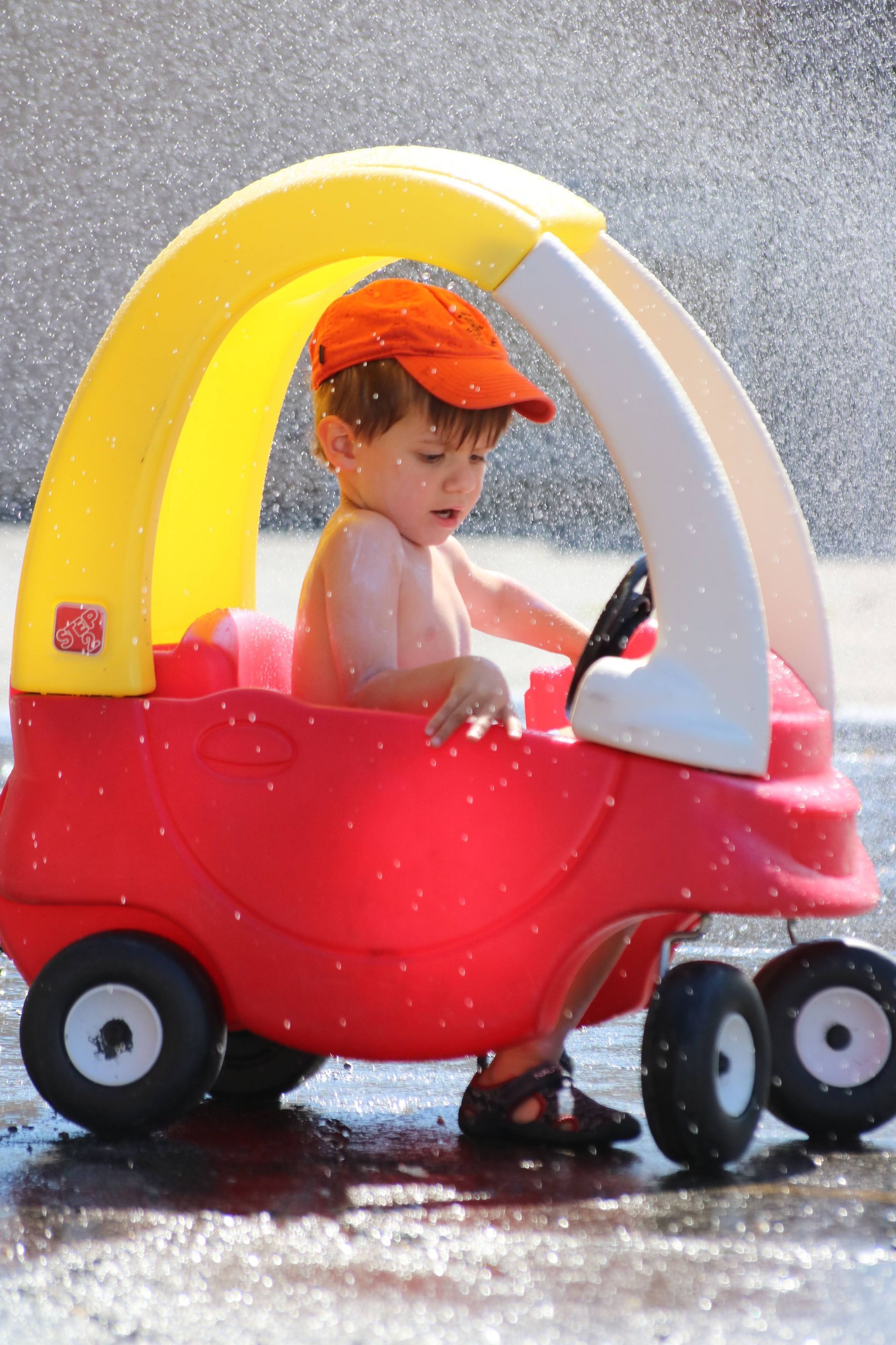 A little boy is playing in a red and yellow toy car