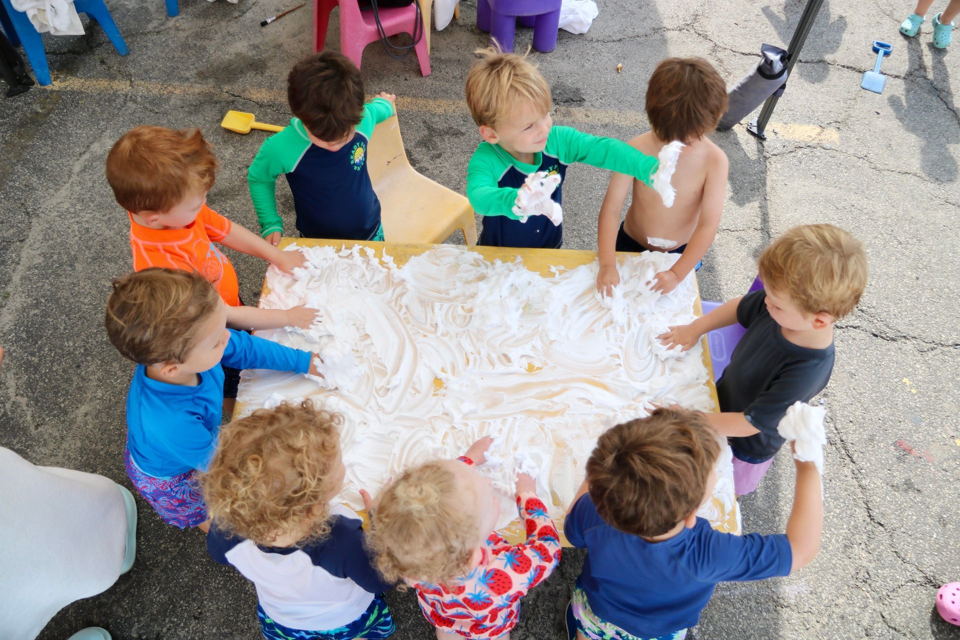 A group of children are playing with shaving cream on a table.