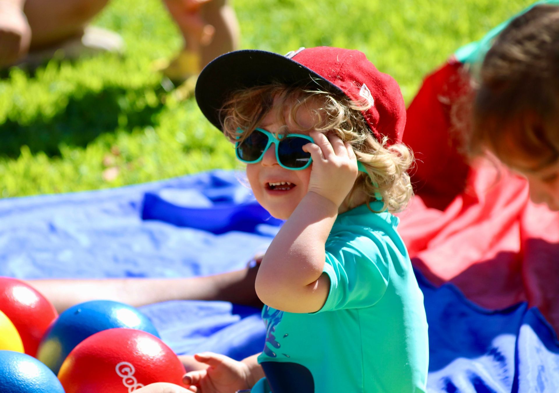 A little boy wearing sunglasses and a hat is playing with balls.