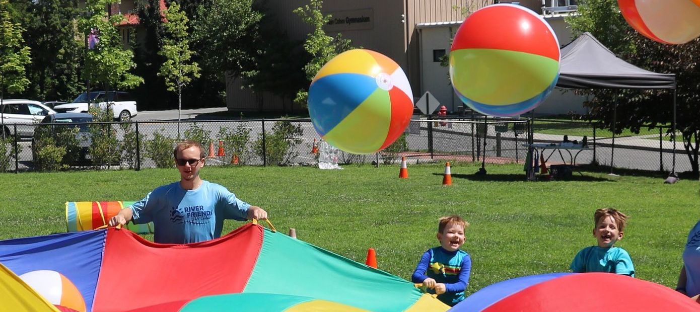 A group of children are playing with parachutes and beach balls