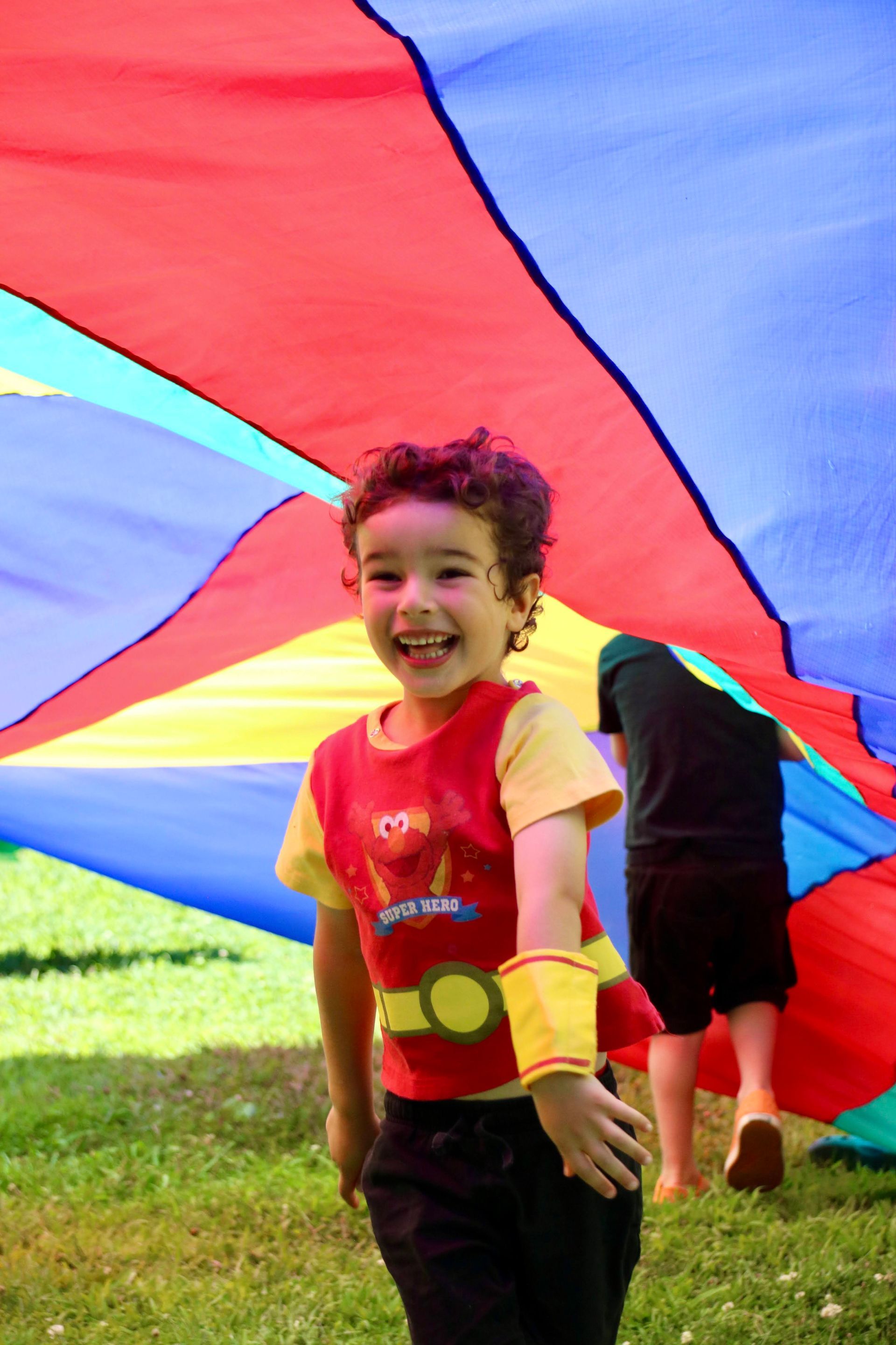 A young boy is standing under a colorful parachute.