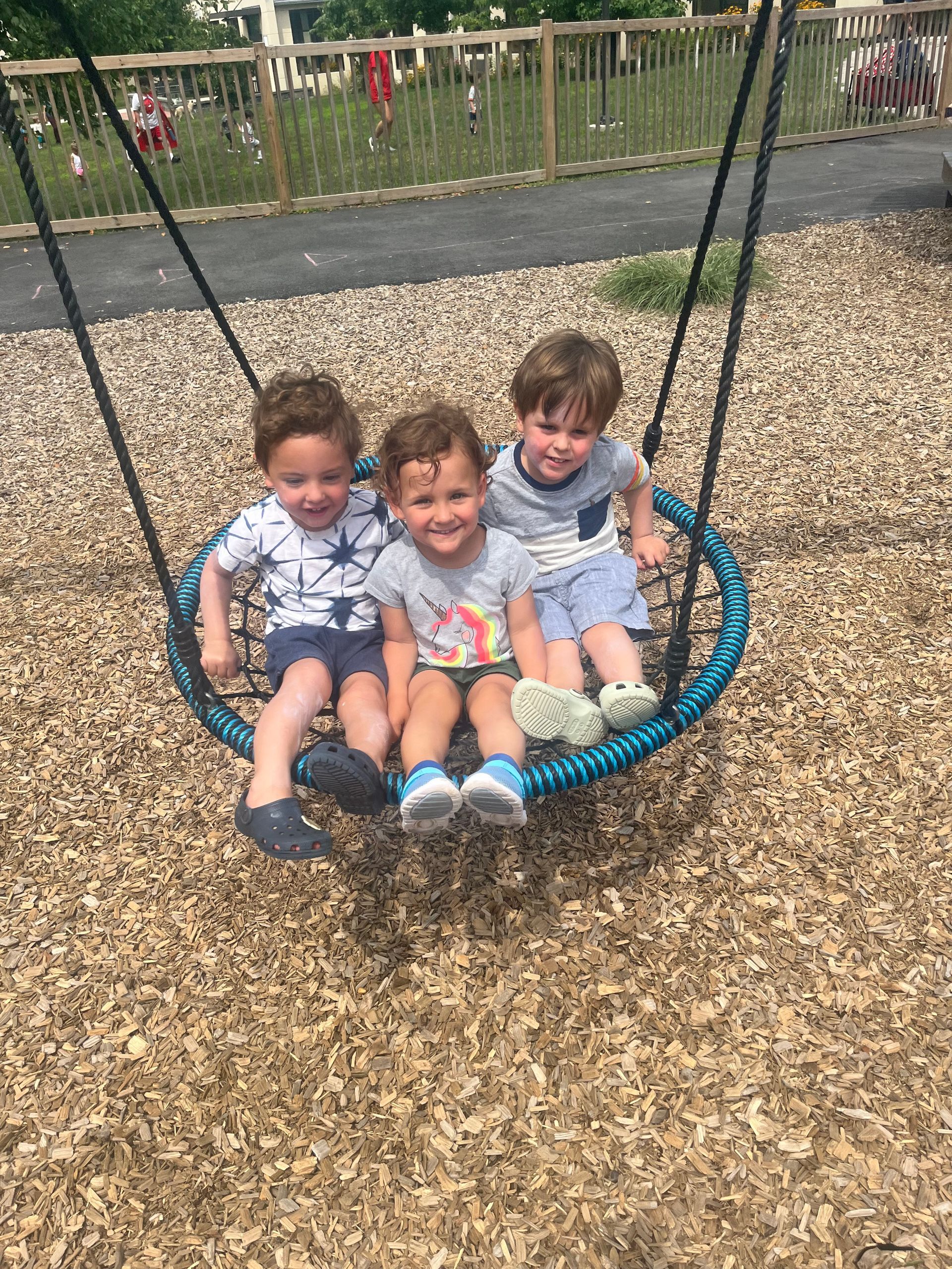 Three young boys are sitting on a nest swing at a playground.