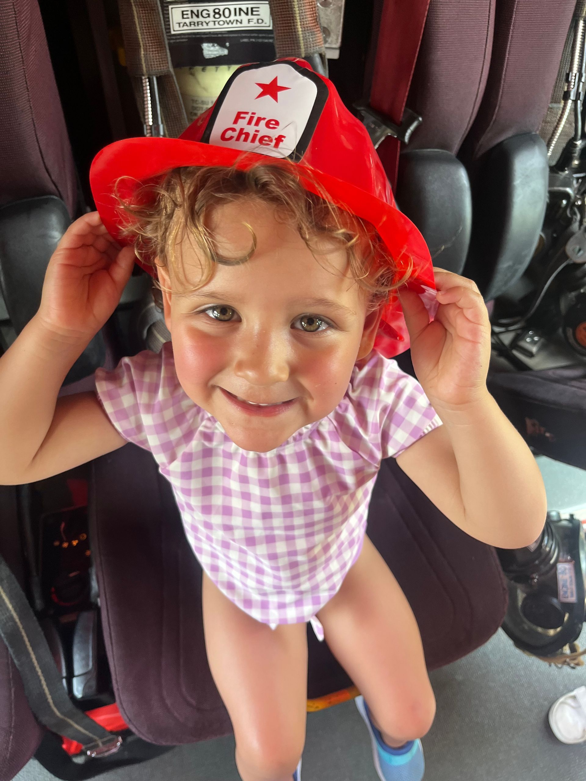 A little girl wearing a red fire chief hat