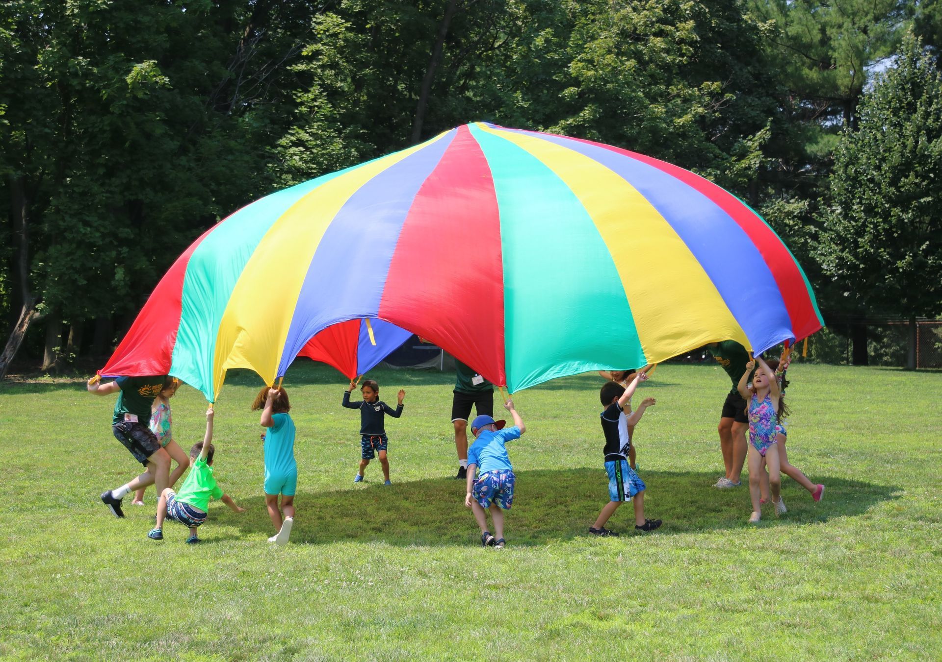 A group of children are playing with a colorful parachute in a field.