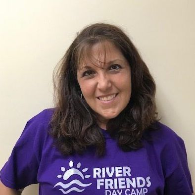 A woman wearing a purple river friends day camp shirt is smiling.