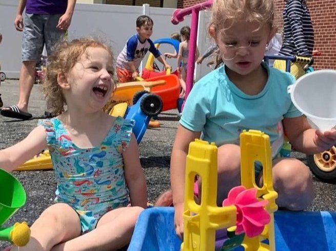Two little girls are sitting on the ground playing with water toys.