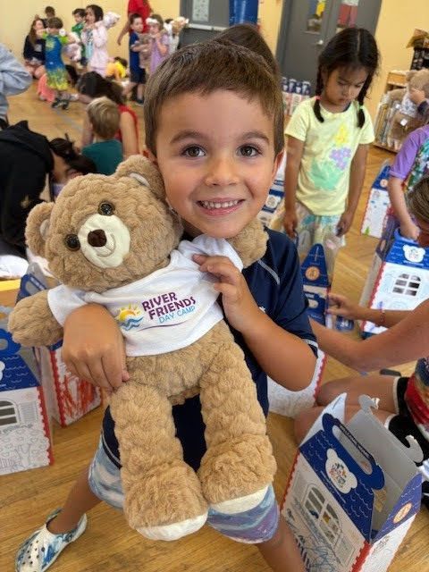 A young boy is holding a teddy bear wearing a riverfront shirt.