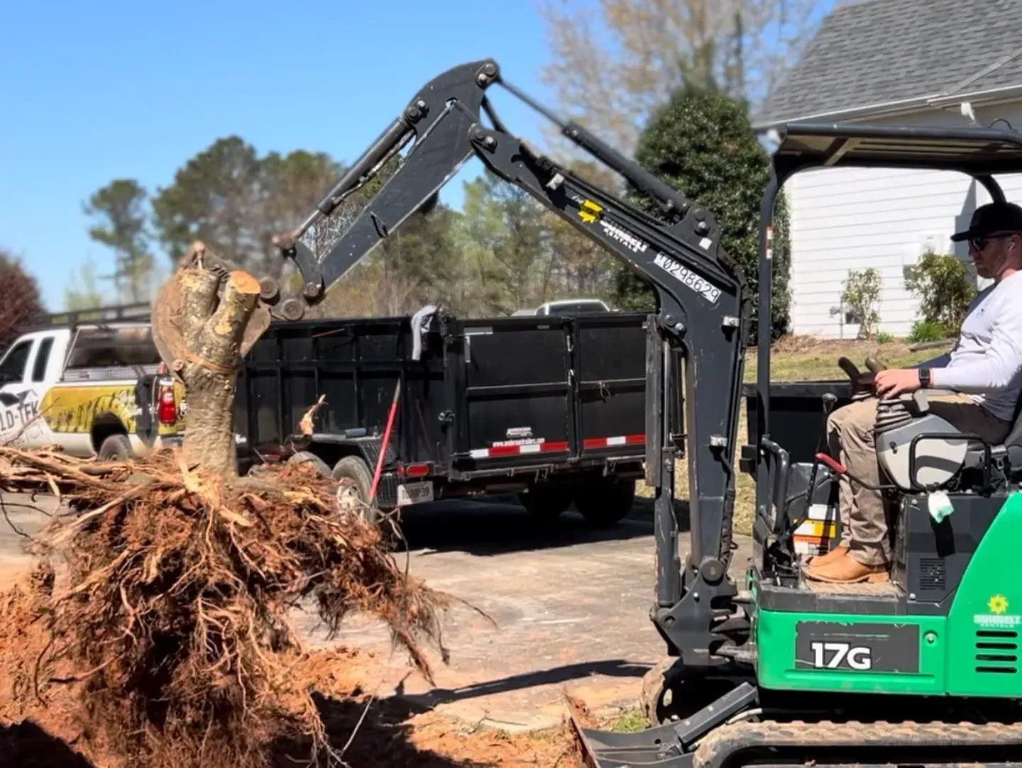 A man is driving a small excavator in a driveway.
