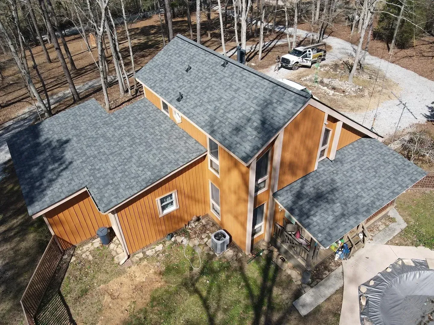 An aerial view of a house with a black roof surrounded by trees.