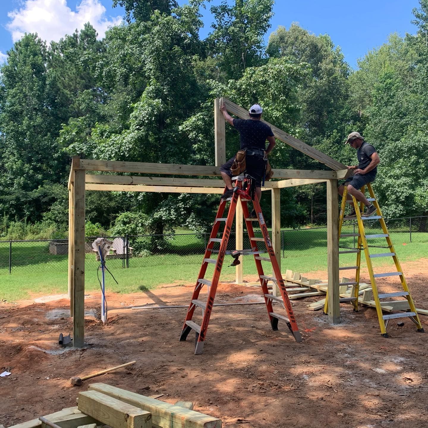Two men are standing on ladders working on a wooden structure.