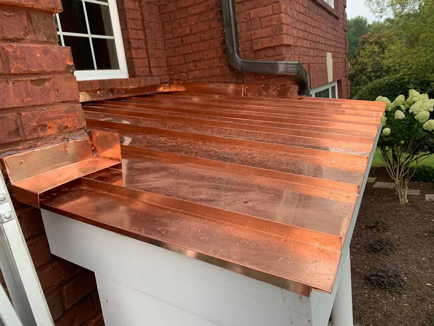 A copper roof is being installed on the side of a brick house.